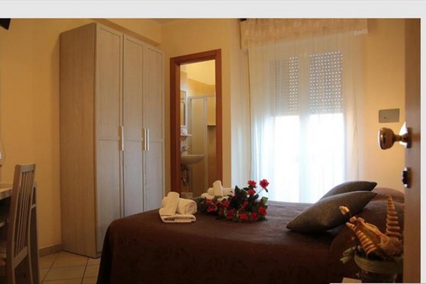 Pokoj s postelí, květinami, skříní a pohledem do koupelny.