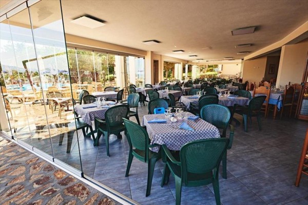 Restaurace se stolky pokrytými modro-bílými ubrusy a zelenými židlemi, s výhledem ven přes skleněnou stěnu.