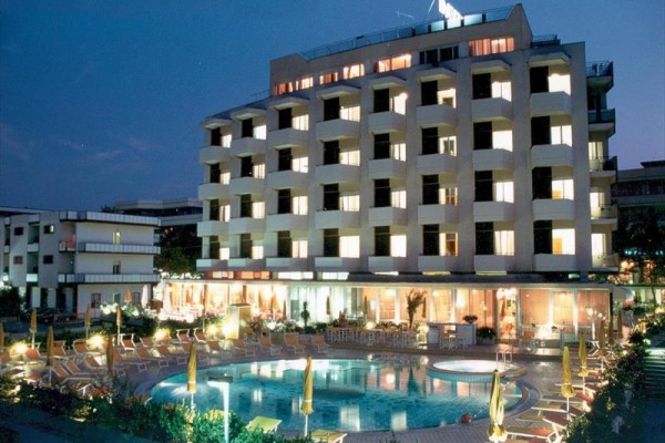 Hotel s osvětlenými okny a venkovním bazénem ve večerních hodinách.