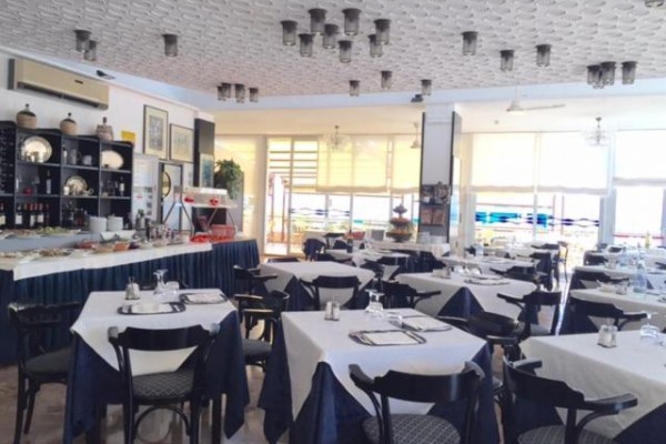 Restaurace s prostřenými stoly, tmavými židlemi a dekorem na stěnách.