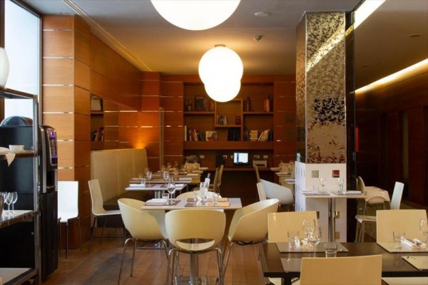 Moderní restaurace s dřevěnými stěnami, policemi s knihami a kulatými závěsnými světly.