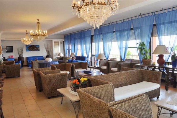 Elegantní obývací pokoj s ratanovými pohovkami, modrými závěsy a křišťálovými lustry.