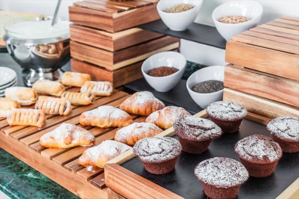 Pečivo s cukrem, muffiny a misky se semínky na dřevěném stojanu.