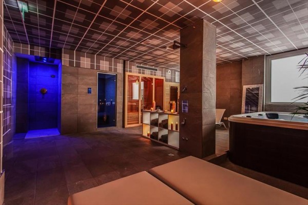 Wellness prostor s vířivkou, sprchou a saunou s tlumeným osvětlením.