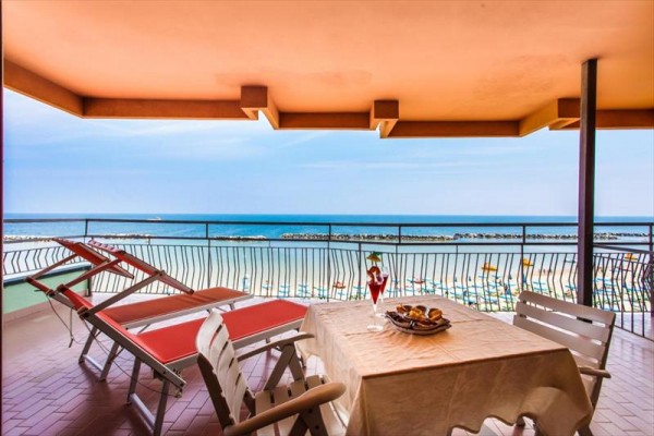 Balkon s výhledem na pláž a moře, stolkem a lehátky.