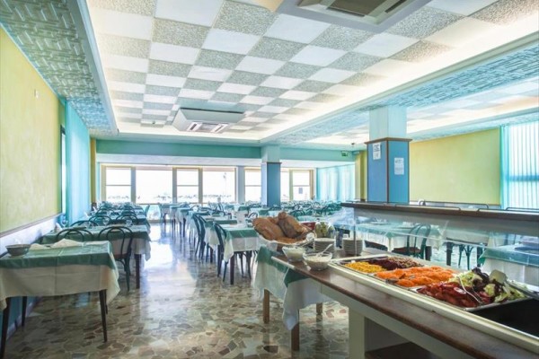 Prázdná restaurace s řadami stolů a bufetovým stolem s jídlem v popředí.