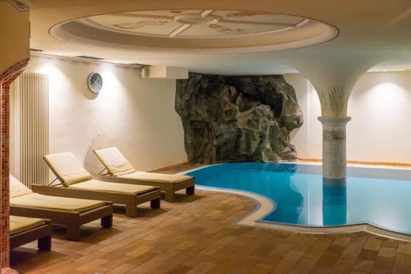 Krytý bazén s lehátky a umělou skalní dekorací.