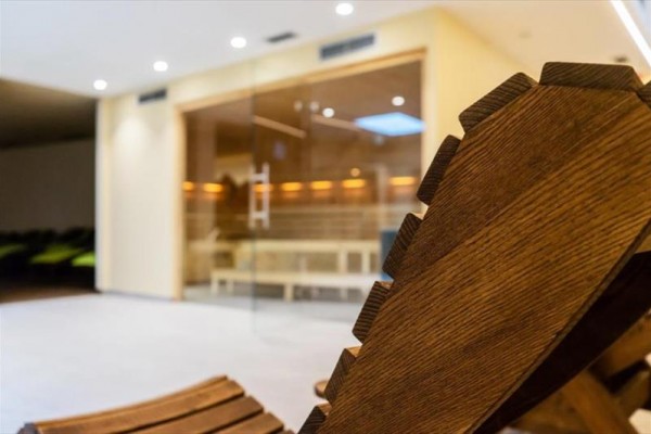 Dřevěné lehátko v prostoru před prosklenou saunou.