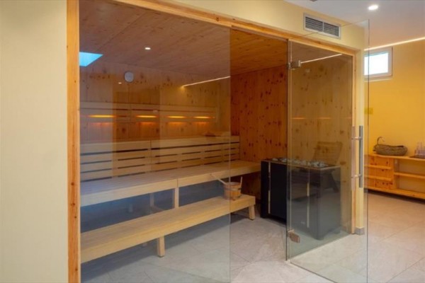 Moderní sauna s dřevěnými lavicemi a skleněnými dveřmi.