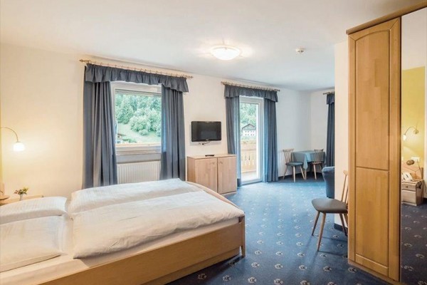 Světlý pokoj s dvojlůžkem, televizí a balkonem, s výhledem na zelenou krajinu.