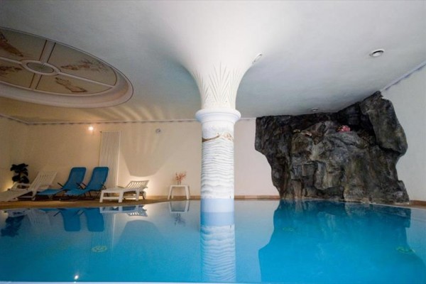 Vnitřní bazén s lehátky a dekorační skálou.