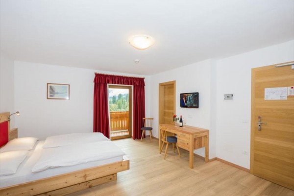 Hotelový pokoj s manželskou postelí, psacím stolem a francouzským oknem na balkon.