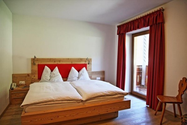 Dvoulůžková postel v hotelovém pokoji s červenými závěsy u balkonu.