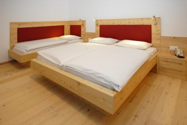 Pokoj s dvěma dřevěnými postelemi s bílým ložním prádlem a červenými čely.