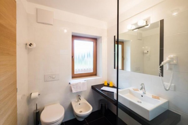 Koupelna s toaletou, bidetem, umyvadlem a zrcadlem vedle okna.