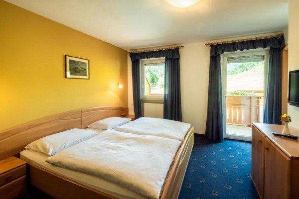 Pokoj s velkou postelí, žlutou stěnou a balkonem s výhledem do přírody.