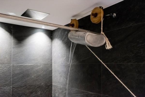 Zavěšené kovové zařízení se dvěma kladkami a lanem nad dlaždicemi v koupelně.  