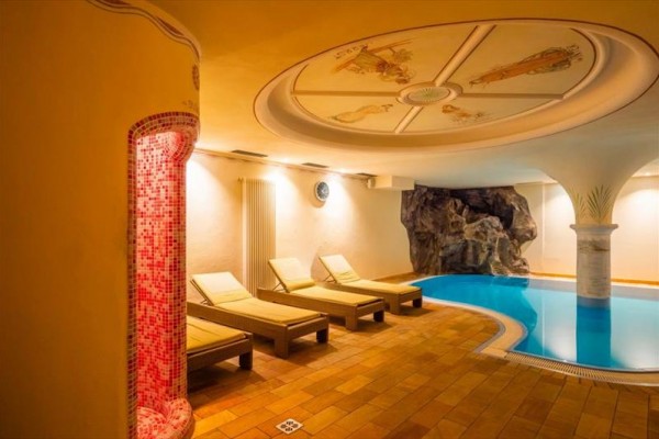 Relaxační zóna s lehátky a bazénem v interiéru s dekorativním stropem.