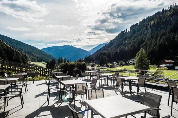 Horská terasa s prázdnými stolky a židlemi s výhledem na lesy a údolí.