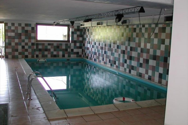 Vnitřní bazén s mozaikovými kachličkami na stěnách a kruhovým záchranným kruhem na vodě.