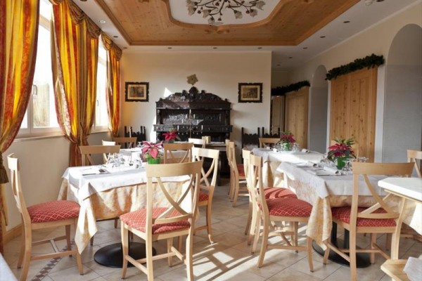 Restaurace s dřevěnými židlemi a ubrusy na stolech, ozdobená vánočními rostlinami.