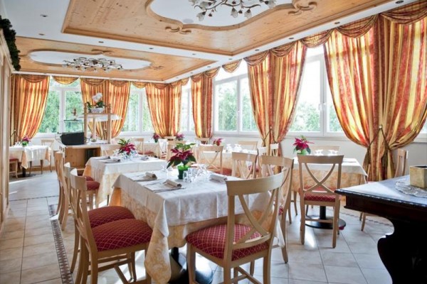 Prostorná restaurace s elegantním dřevěným stropem a červeno-žlutými závěsy.