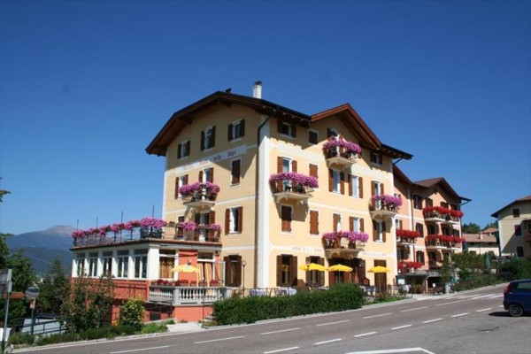 Třípatrový hotel s balkony ozdobenými květinami u silnice za slunečného dne.
