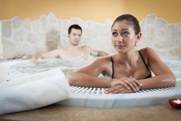 Dva lidé relaxují ve vířivce obklopení kamennou zdí.