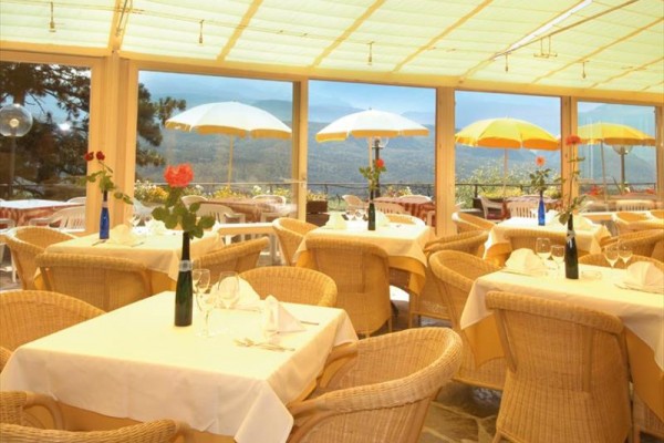 Elegantní restaurace s proutěným nábytkem a výhledem na hory skrze velká okna.
