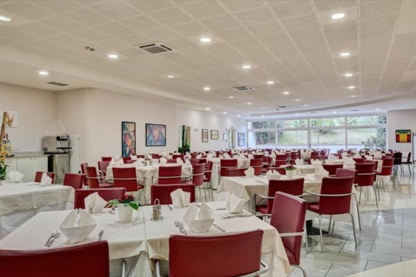 Jídelna s červenými židlemi a bílými ubrusy, připravená na hosty.