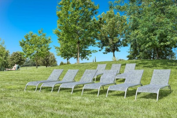 Osm lehátek postavených na trávníku s pozadím stromů a jasné oblohy.