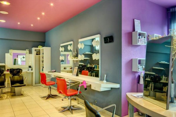 Interiér kadeřnického salónu s fialovými a šedými stěnami, červenými židlemi a zrcadly.