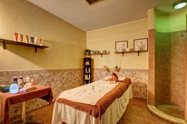 Pokoj pro masáže s masážním stolem a regály s kosmetikou.