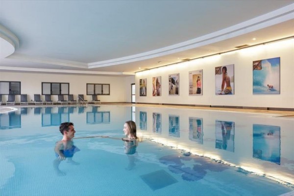 Dva lidé v krytém bazénu poblíž zdi s fotografiemi.  