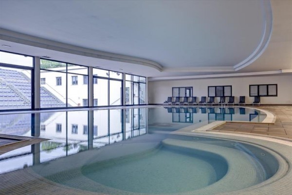 Krytý bazén s vířivkou a řadou prázdných lehátek u stěny.