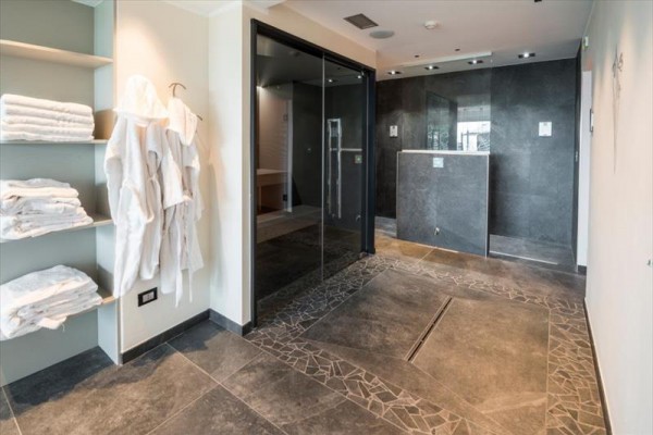 Moderní wellness prostor s regálem plným ručníků a župany pověšenými na stěně.