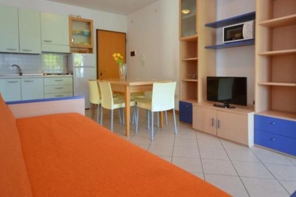 Obývací pokoj s oranžovou pohovkou, kuchyňským koutem a jídelním stolem.