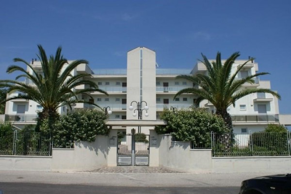 Moderní vícepatrová budova se dvěma palmami u vchodu.