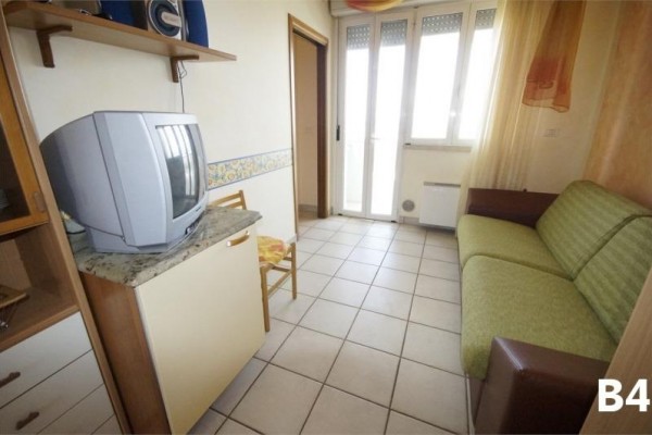 Malý pokoj s pohovkou, televizorem a balkonovými dveřmi.