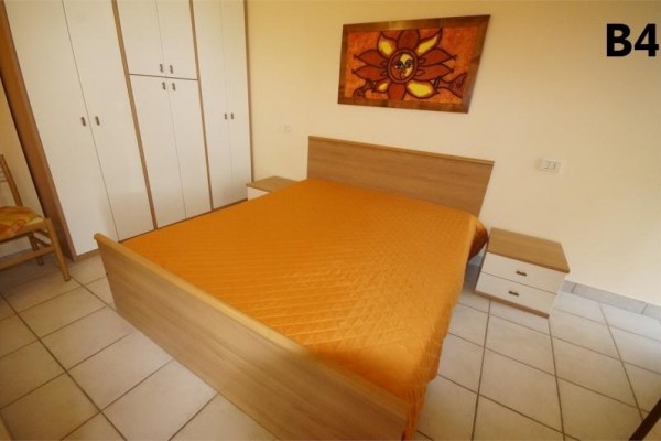 Ložnice s dvoulůžkem, oranžovým přehozem a obrazem slunce nad postelí.