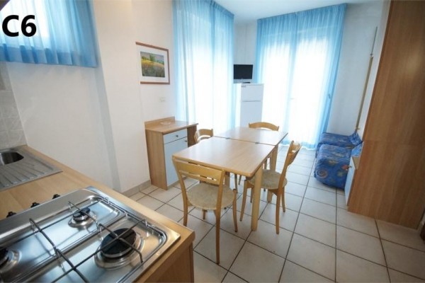 Kuchyň s jídelním stolem a židlemi, vedle které je pohovka a okno s modrými závěsy.