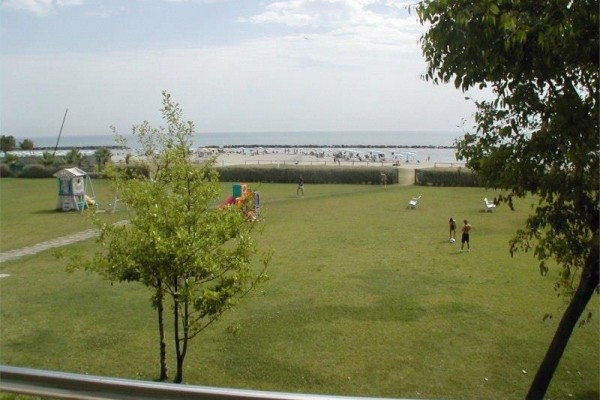 Přímořská pláž s lidmi a zeleným trávníkem v popředí.