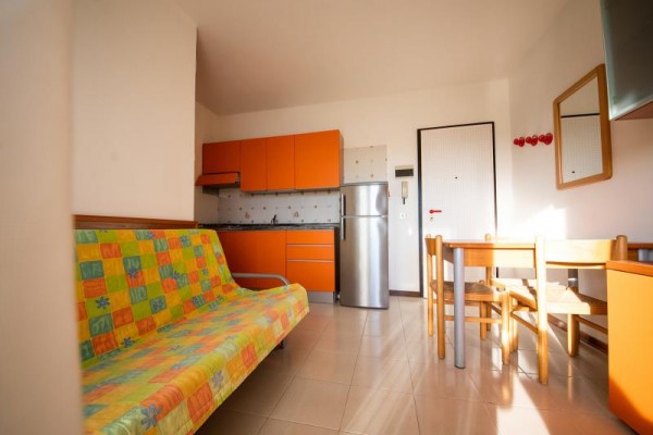 Moderní kuchyň s oranžovými skříňkami a pohovkou s barevným přehozem.