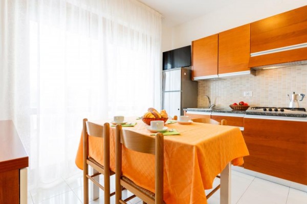 Světlá kuchyně s dřevěným nábytkem a prostřeným stolem s oranžovým ubrusem.