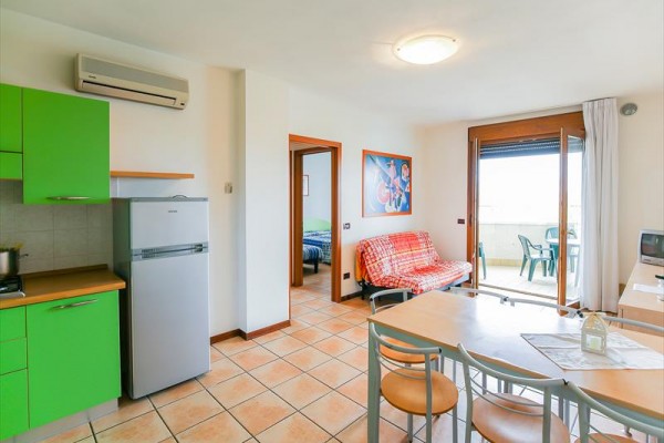Moderní obývací pokoj s kuchyní v zelených barvách, sedačkou a přístupem na balkon.  