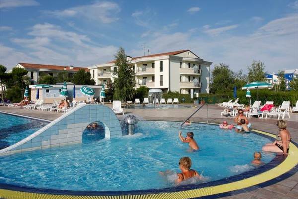 Lidé si užívají venkovní bazén u rezidenčního komplexu s lehátky a slunečníky okolo.