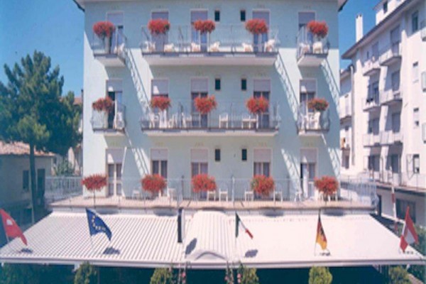 Budova hotelu s balkóny ozdobenými červenými květinami a vlajkami nahoře.