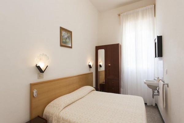 Jednoduše zařízený pokoj s manželskou postelí, skříní, umyvadlem a stropním ventilátorem.