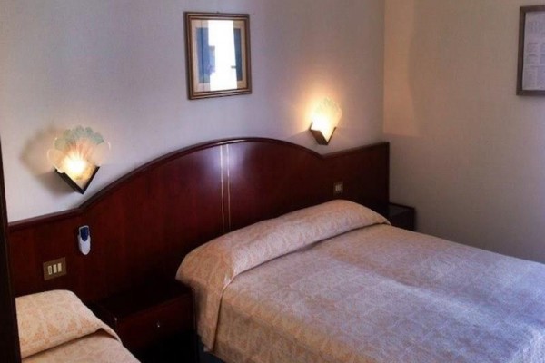 Pokoj s manželskou postelí a jednolůžkem, osvětlený dvěma nástěnnými lampami.