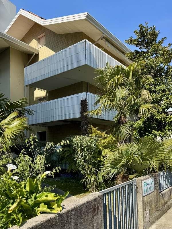 Moderní dům s velkými balkony obklopený tropickou vegetací.